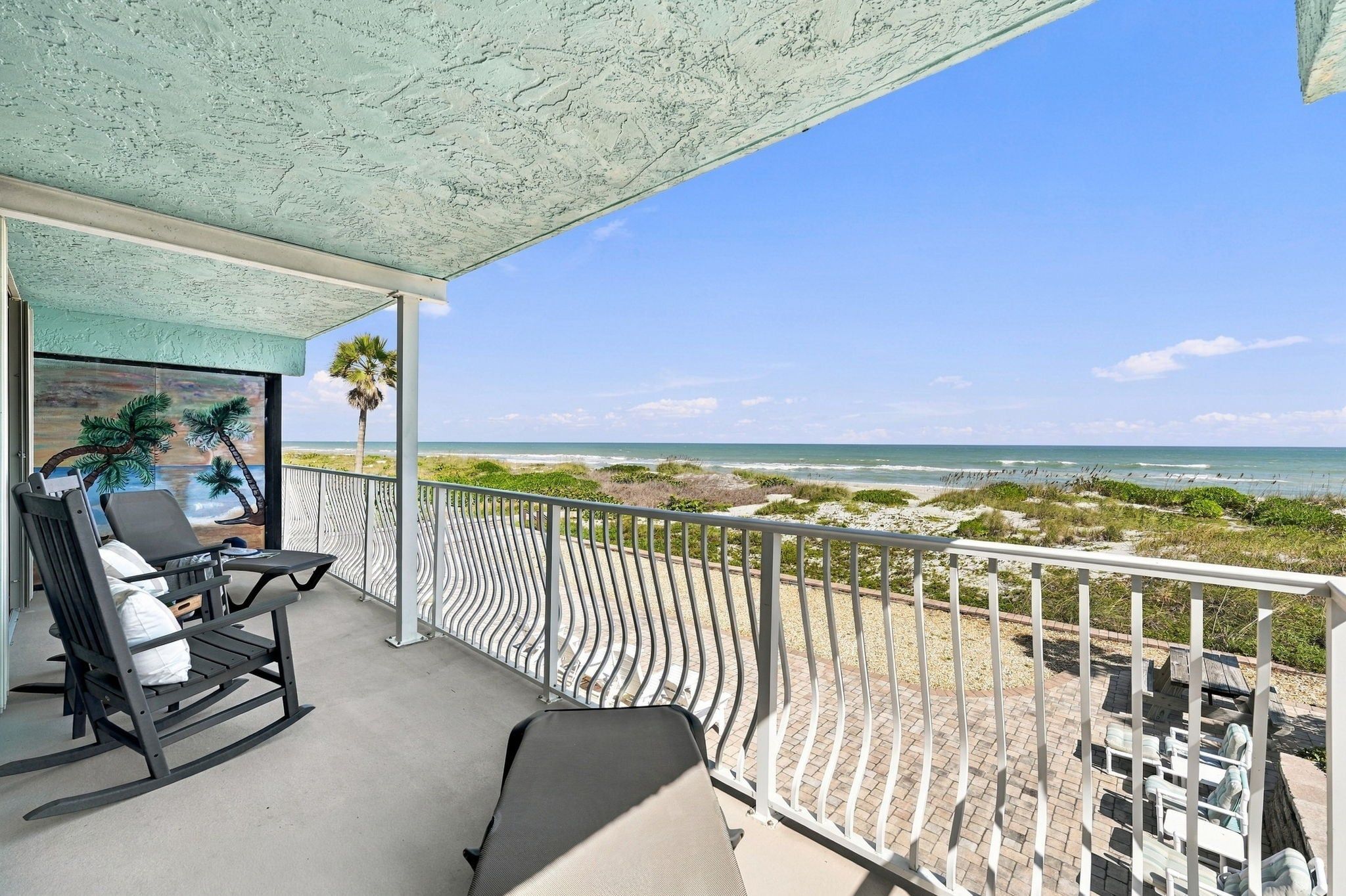 Un balcon avec vue sur la plage, équipé d’un fauteuil à bascule et d’une table.