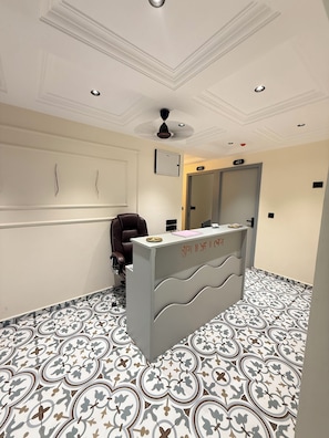 A reception desk with a number sign, a brown chair, and patterned floor tiles. - Hotel Pacific Comfort (Ahmedabad)