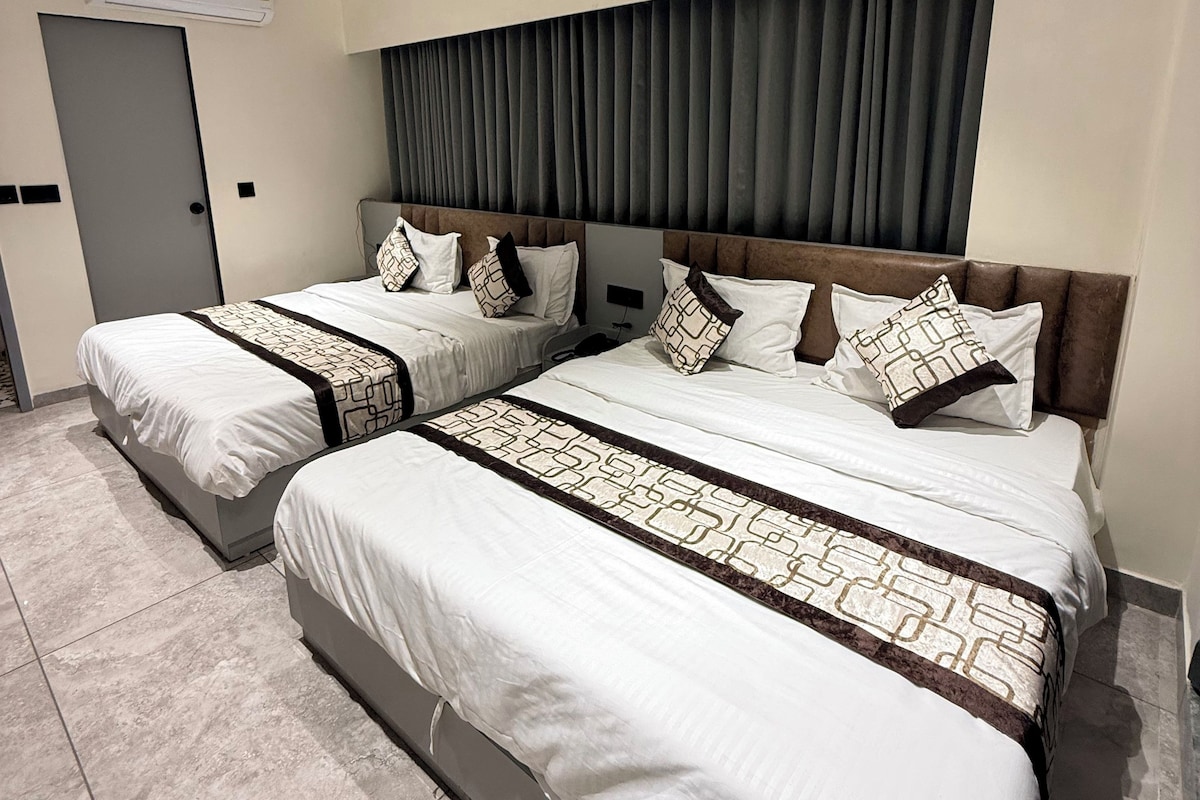 A hotel room with two beds, a ceiling fan, an air conditioning unit, and a large window with curtains.