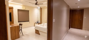 A hotel room with a bed, a desk, a chair, a ceiling fan, a clock, and a door. - GATEWAY CONTINENTAL EXPRESS (Kolkata)