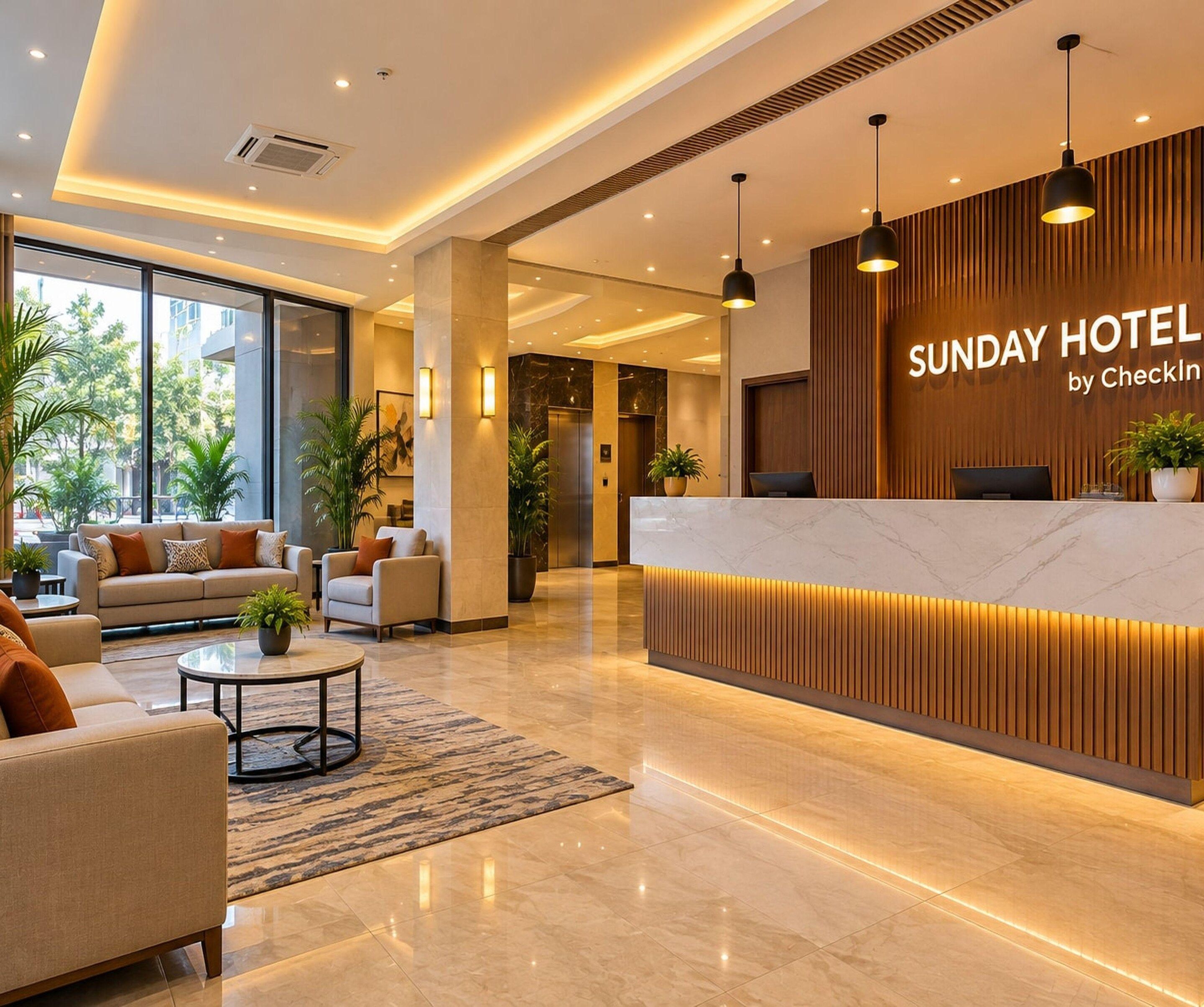 Et hotellets reception område med et moderne design, med en receptionsdisk, siddeområde med sofaer, og et stort vindue der giver udsigt til det fri.