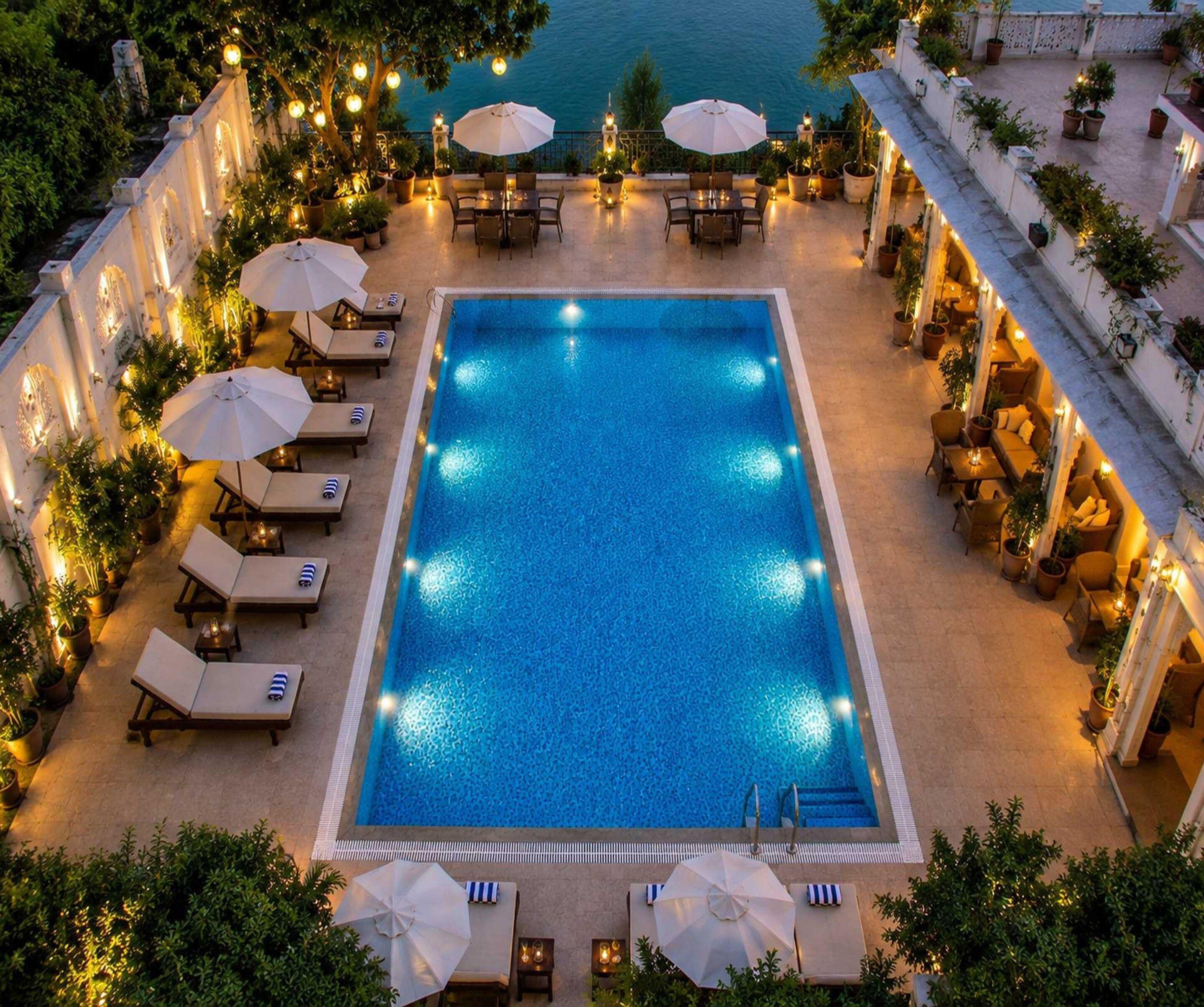 A rectangular swimming pool surrounded by lounge chairs and umbrellas, with a view of the sea in the background.