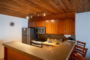 A kitchen with wooden cabinets, stainless steel appliances, granite countertops, and a wooden ceiling. - Snowbird Iron Blosam Lodge - Bedroom and Studio Hotel Apartment (Snowbird)