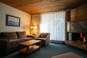 Ein gemütliches Wohnzimmer mit einer Couch, einem Sessel und einem Couchtisch, einem Kamin und einem Bild an der Wand.
