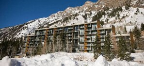 Ein mehrstöckiges Hotel mit modernem Design, gelegen in einer Bergregion mit schneebedeckten Gipfeln im Hintergrund.