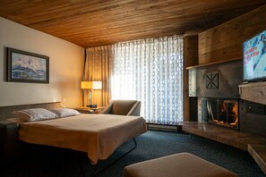 Ein Hotelzimmer mit Bett, Sessel, Fernseher, Kamin und einem Gemälde an der Wand.