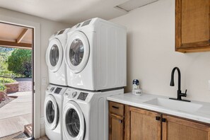 A laundry area with stacked front-loading washers and dryers, a sink, and wooden cabinets. - Sedona Red Rock Retreat for 8 | 2 Homes, 4BR, Sunroom Dining, Game Room, Fire Pit & Private Patios (Sedona)