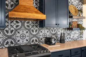 A kitchen with a gas stove, a toaster, a wooden range hood, and patterned backsplash tiles. - Sedona Red Rock Retreat for 8 | 2 Homes, 4BR, Sunroom Dining, Game Room, Fire Pit & Private Patios (Sedona)