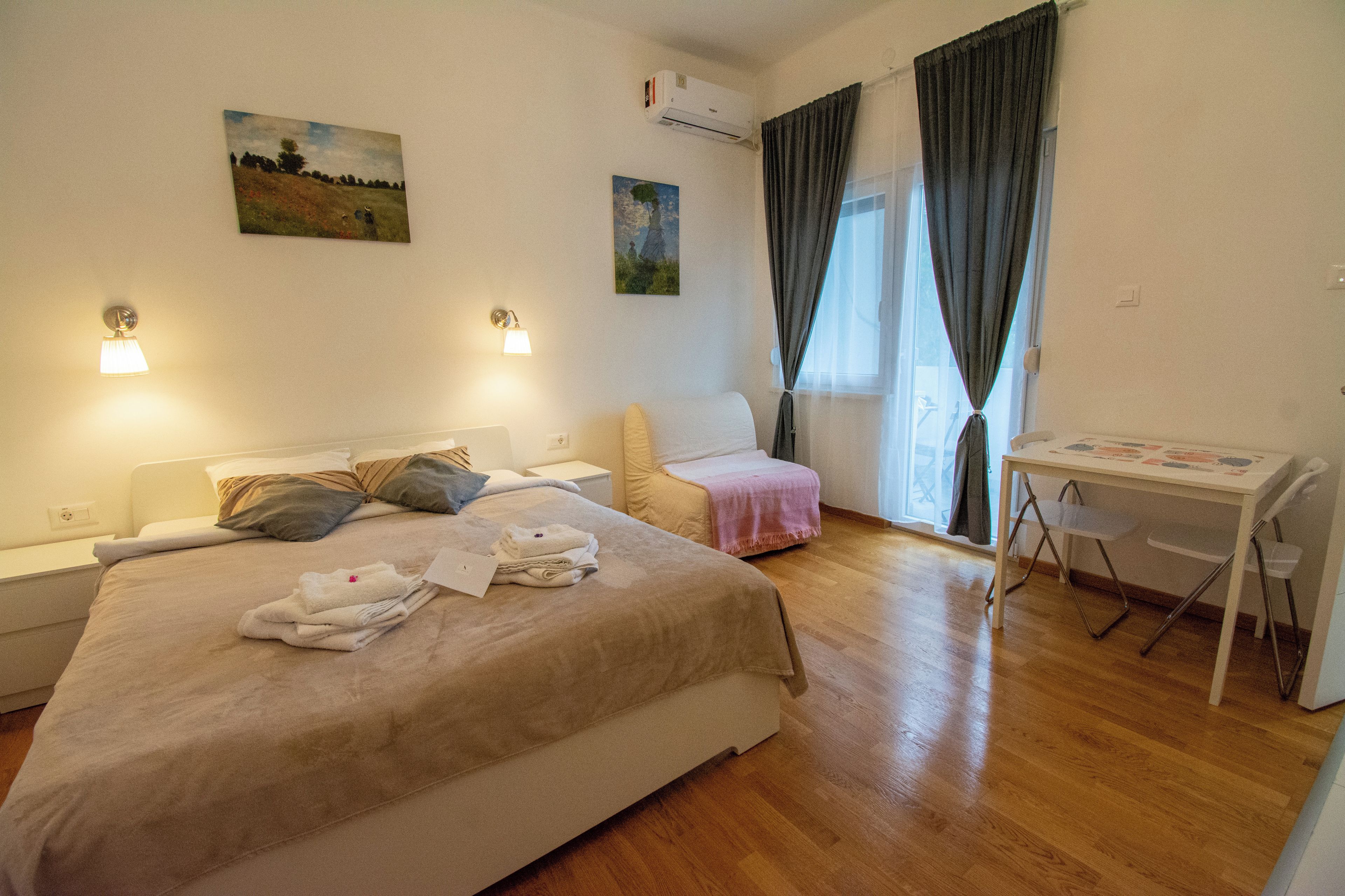 A hotel room with a bed, a desk, a chair, and two paintings on the wall.