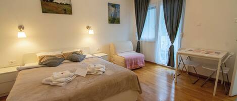 A hotel room with a bed, a desk, a chair, and two paintings on the wall.