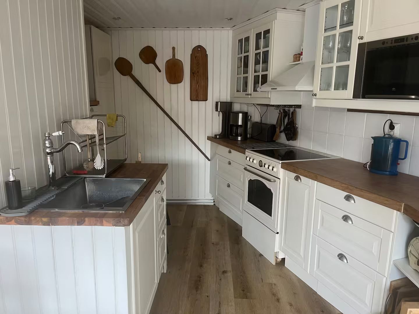 A kitchen with white cabinetry, a wooden countertop, a sink, a stove, and a microwave.