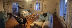 Ett mysigt vardagsrum med en soffa, en gungstol, ett litet bord med en fruktskål och ett fönster med gardiner.