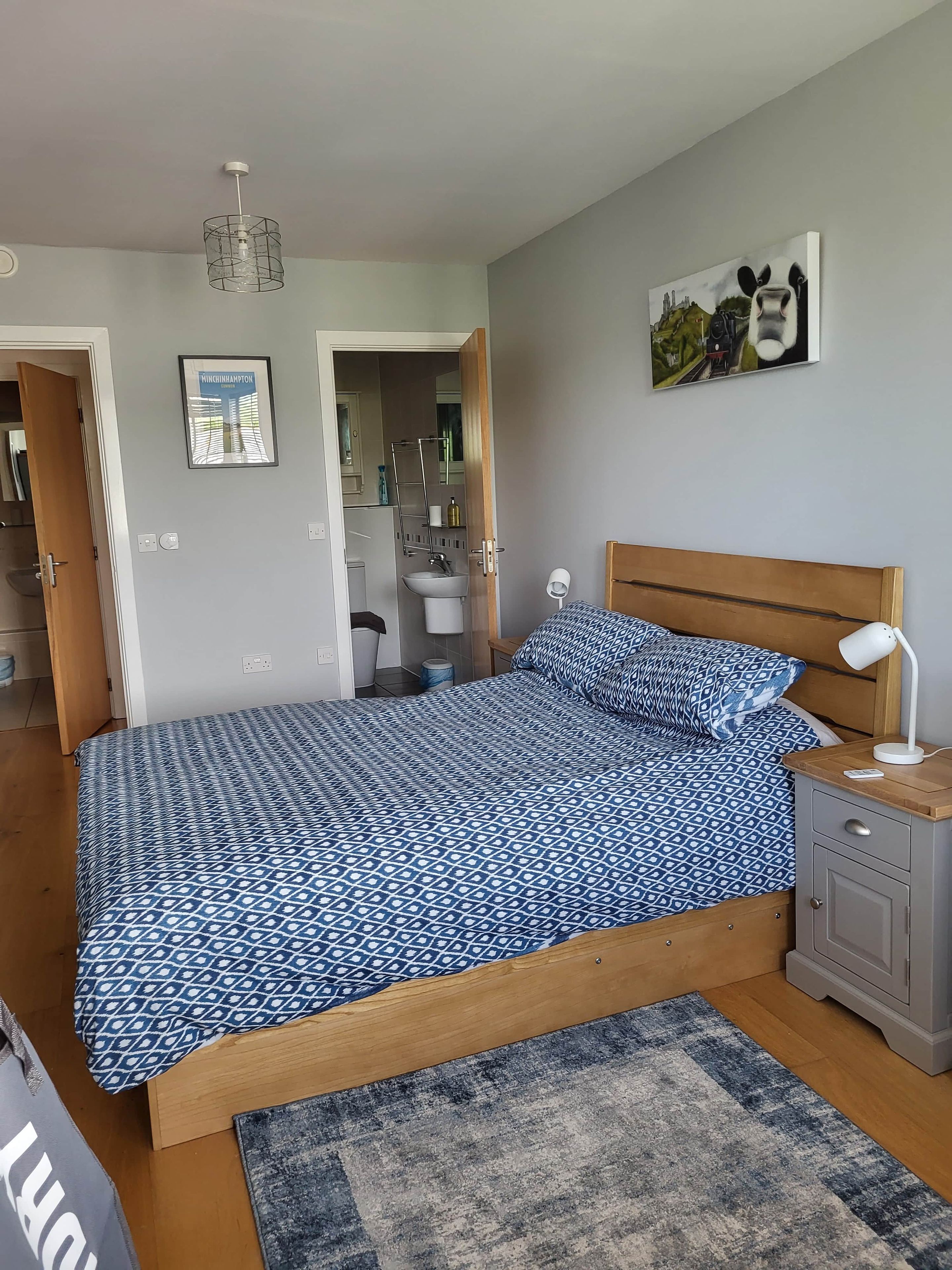 A bedroom with a bed, bedside table, lamp, and a painting on the wall.