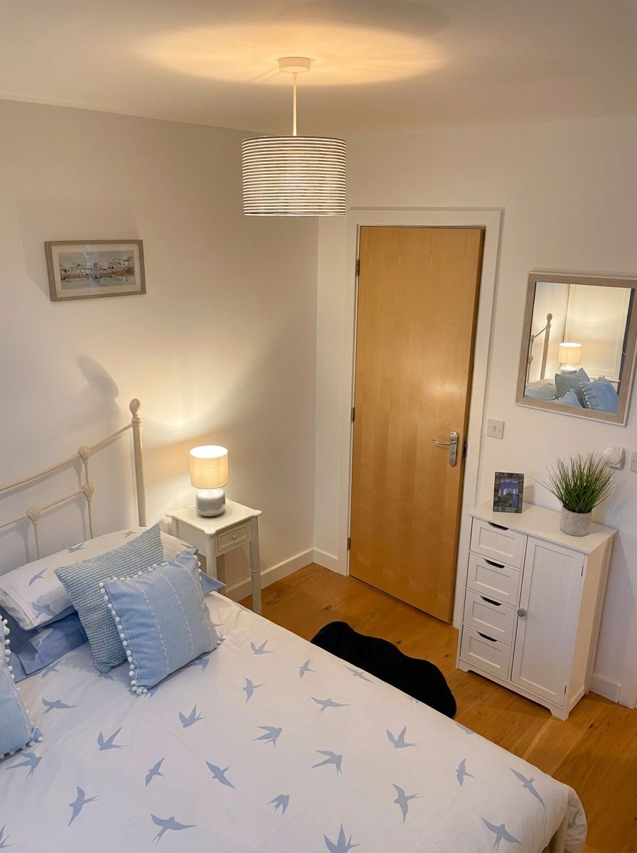 A bedroom with a bed, bedside lamp, wooden door, dresser, and a mirror on the wall.