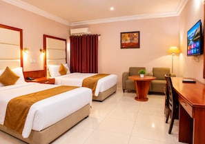 Quarto de hotel com duas camas, uma escrivaninha, uma cadeira, uma televisão e um quadro na parede.