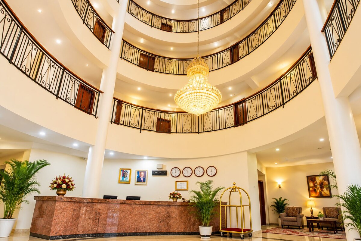 Um hall de hotel amplo em vários níveis, com um lustre imponente, um balcão de recepção e uma área de estar.