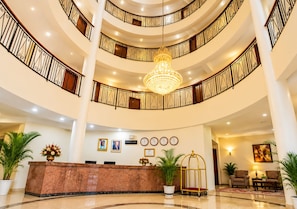 Um hall de hotel amplo em vários níveis, com um lustre imponente, um balcão de recepção e uma área de estar.