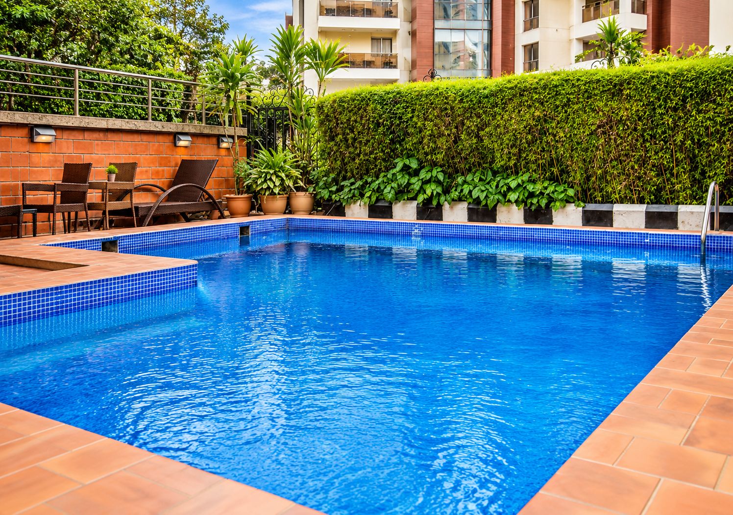 Une piscine rectangulaire aux carreaux bleus, entourée d’une terrasse en briques et agrémentée de plantes en pot.
