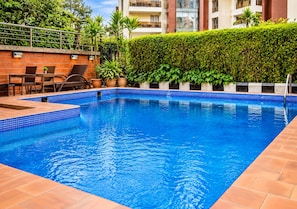 A rectangular swimming pool with blue tiles, surrounded by a brick deck and potted plants. - Denis Hotel Abuja (Abuja)
