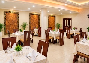 Espaço de refeições de hotel com várias mesas, cadeiras e painéis decorativos na parede.