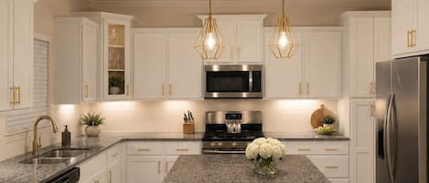 A modern kitchen with white cabinetry, stainless steel appliances, and a central island with two chairs.