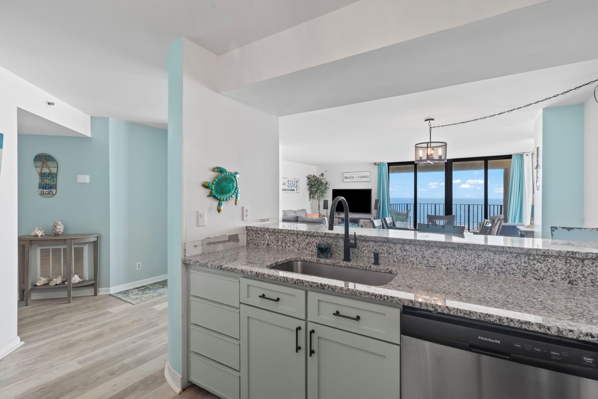 A modern kitchen with granite countertops, a stainless steel dishwasher, and a large window offering a view of the ocean.