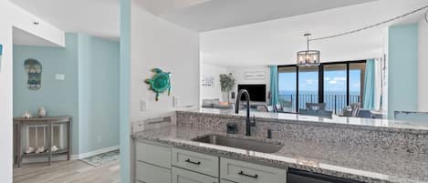 A modern kitchen with granite countertops, a stainless steel dishwasher, and a large window offering a view of the ocean.