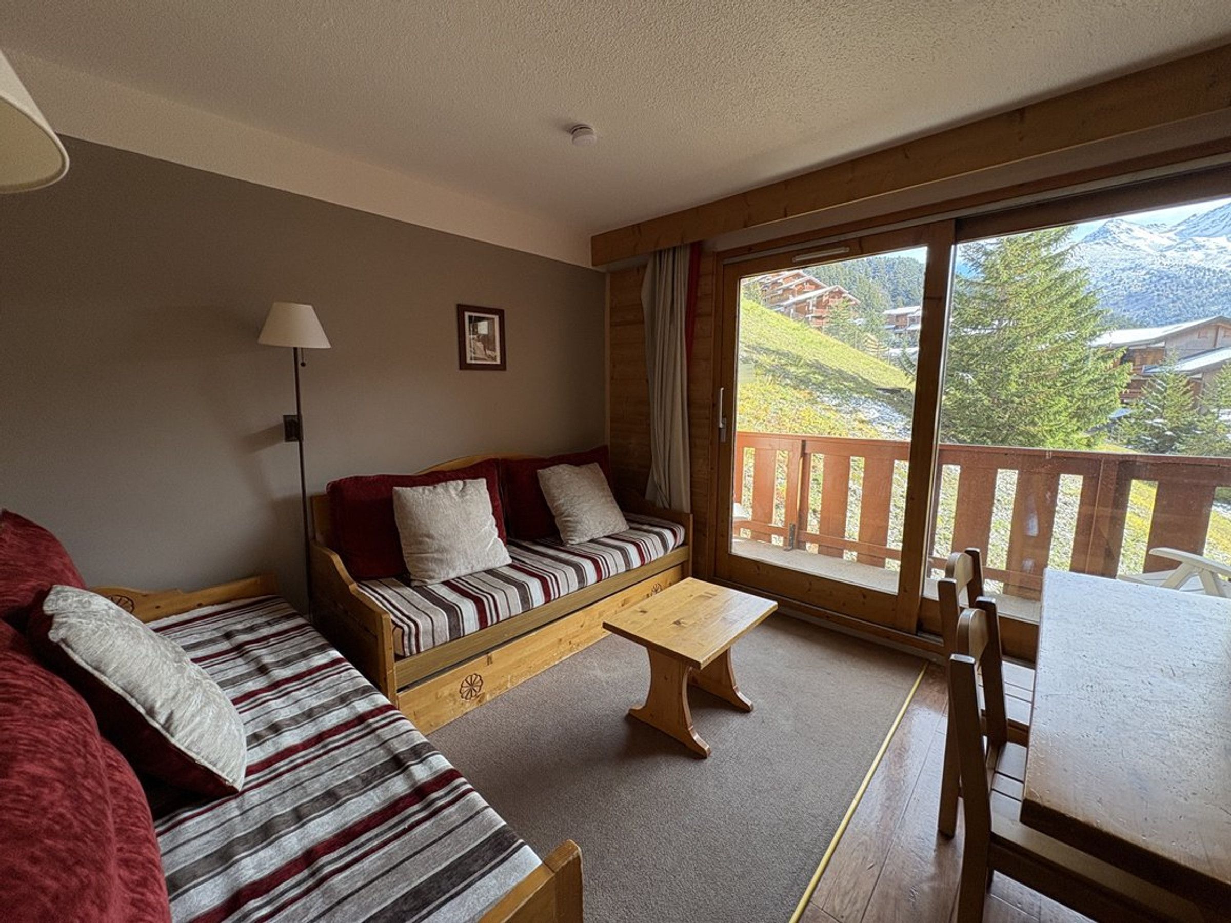 A cozy room with a sofa, a wooden table, and a balcony with a view of the mountains.