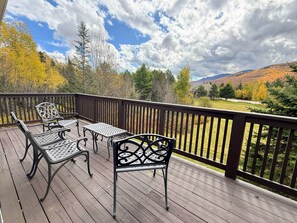 Um deck de madeira com móveis externos e vista para uma paisagem montanhosa.