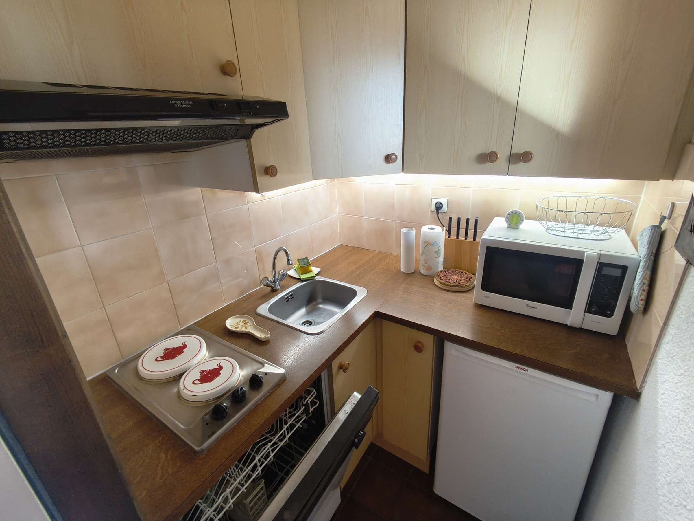 A compact kitchen with a sink, stove, microwave, and a small refrigerator.
