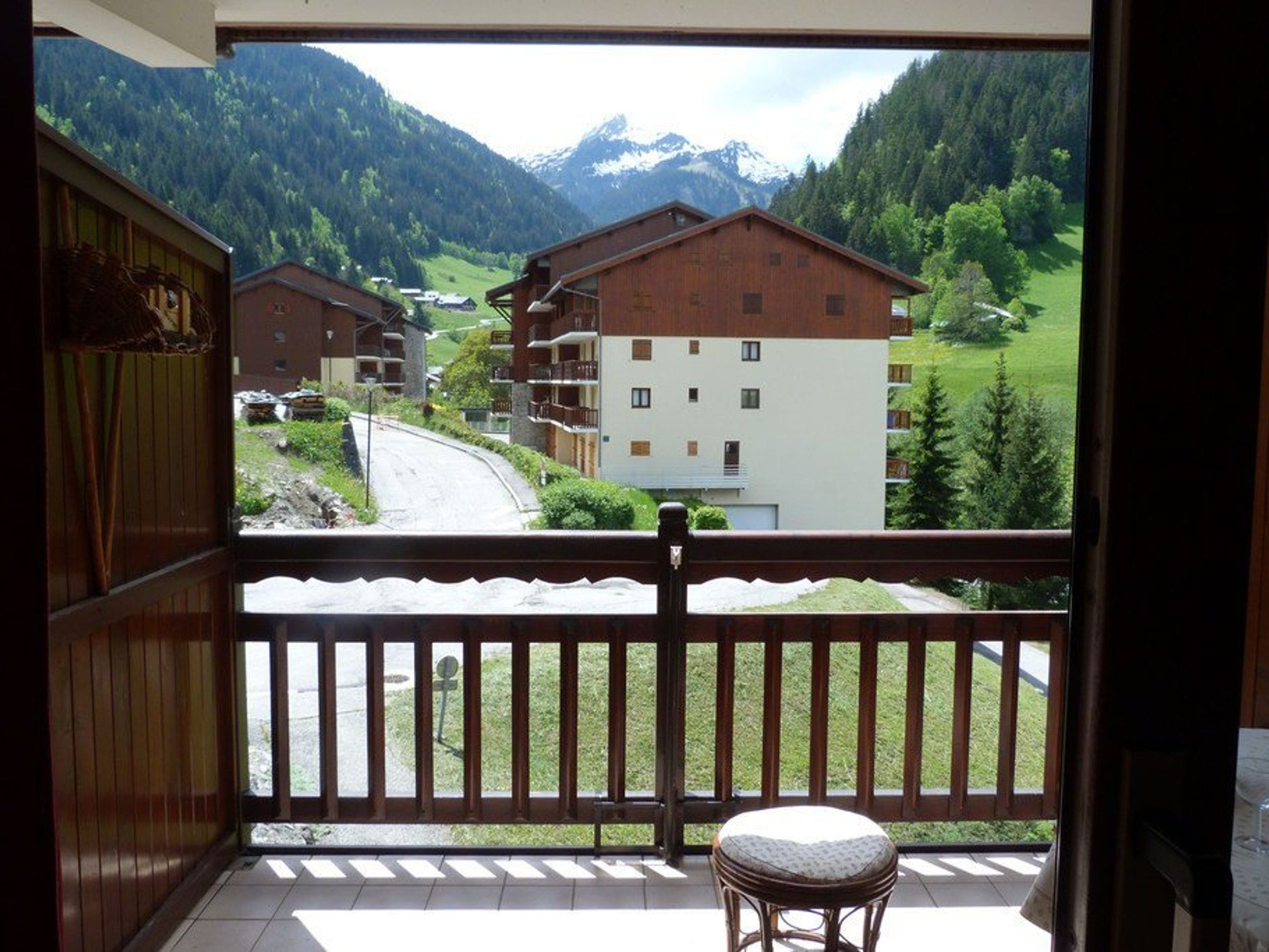 A balcony with a view of a mountain landscape, a wooden railing, and a small stool.