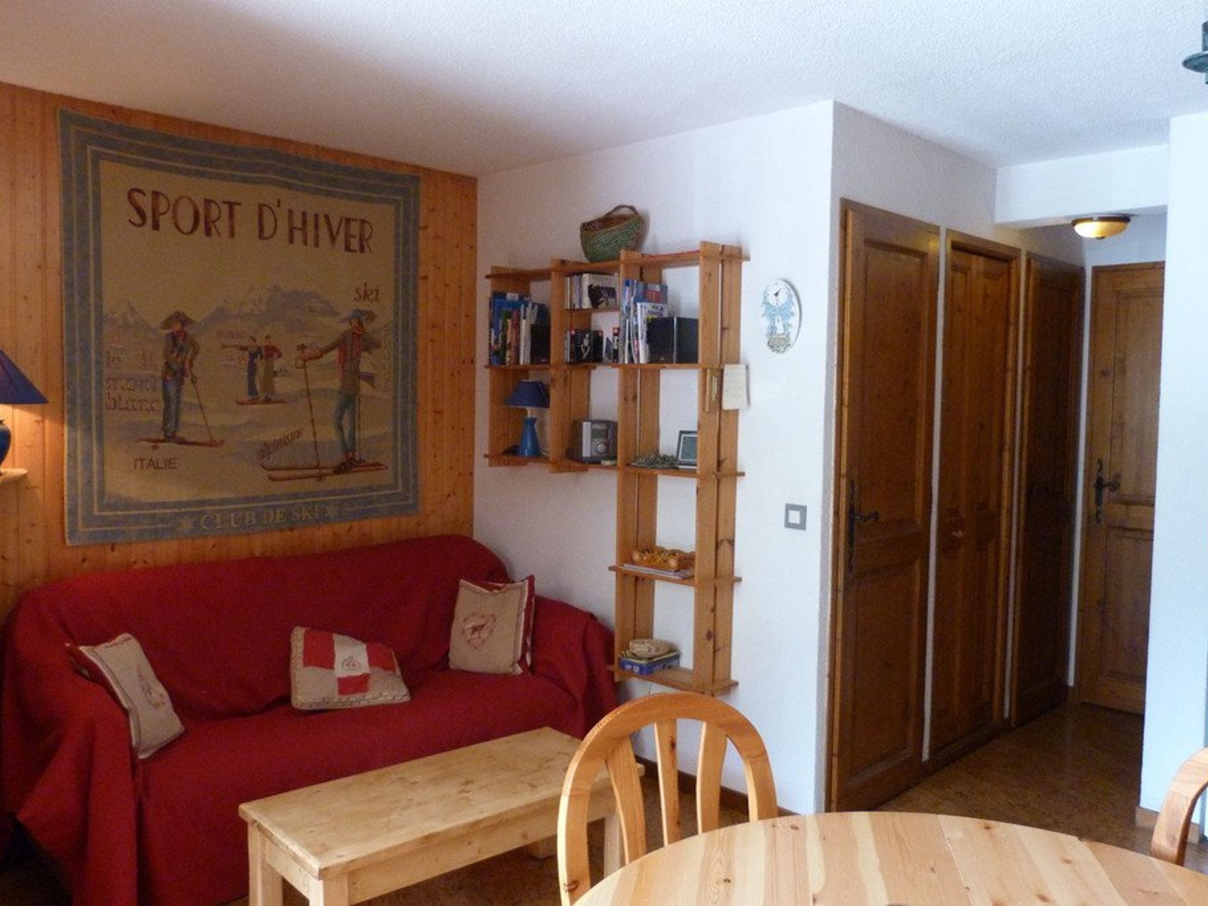 Une pièce avec un canapé rouge, une table en bois et une bibliothèque contenant divers objets.