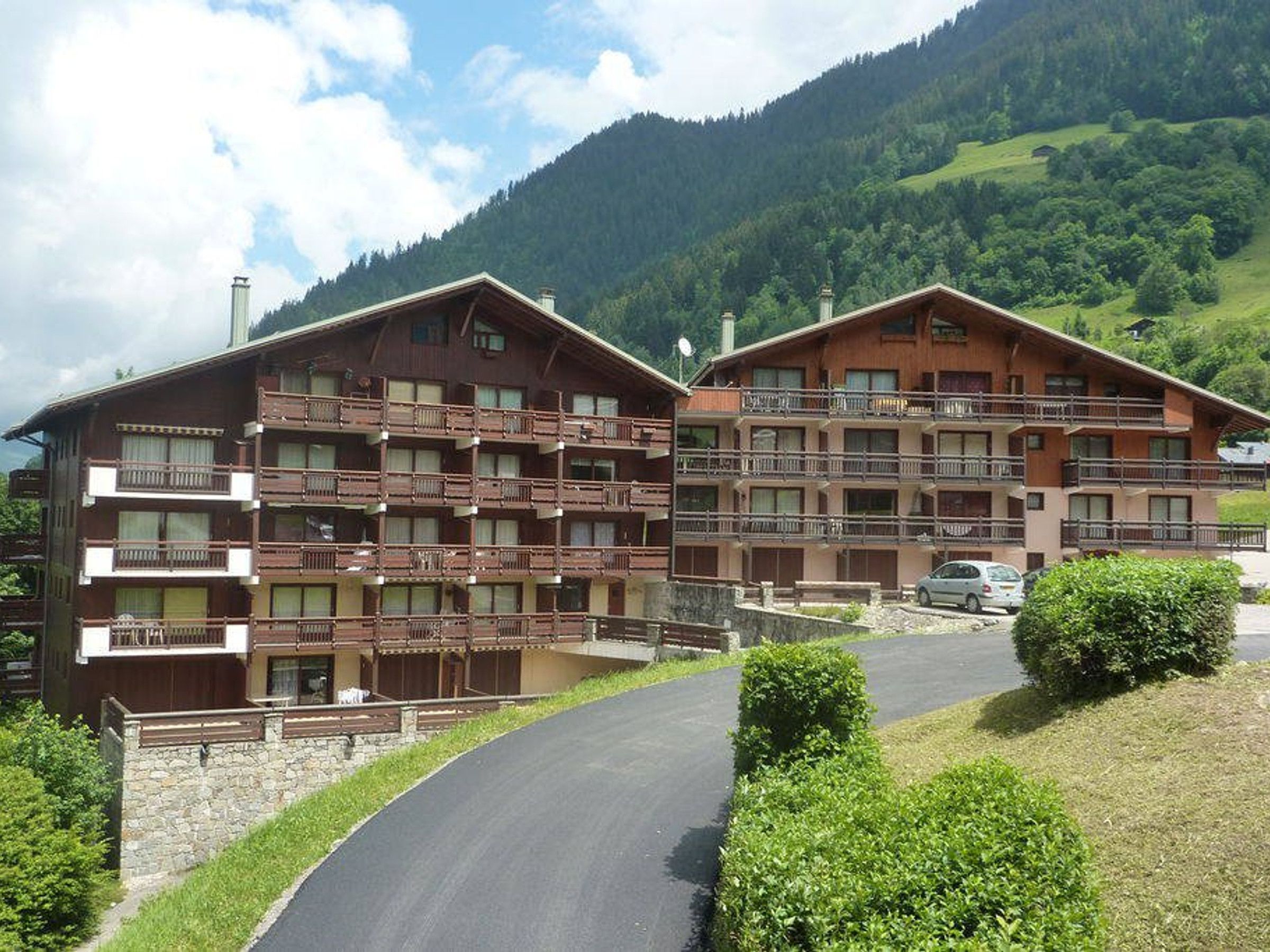 A multi-story hotel with balconies, set against a mountainous backdrop.