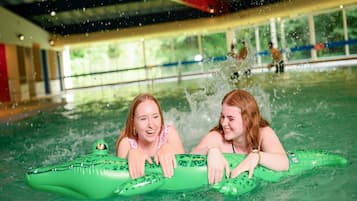 An indoor swimming pool with two individuals on green inflatable swim floats.
