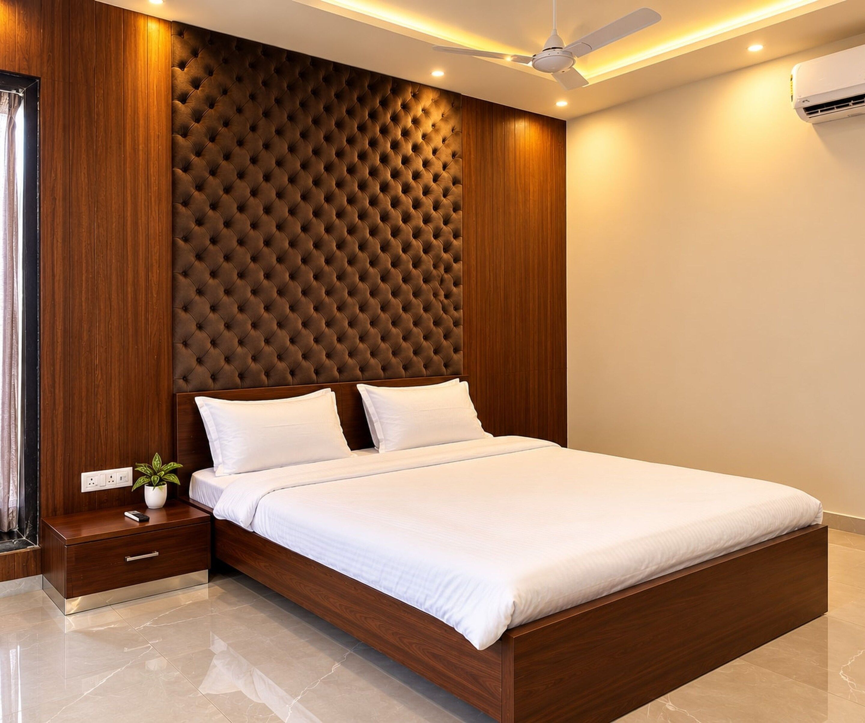 A modern bedroom with a wooden headboard, a bed with white bedding, a nightstand with a plant, and a ceiling fan.