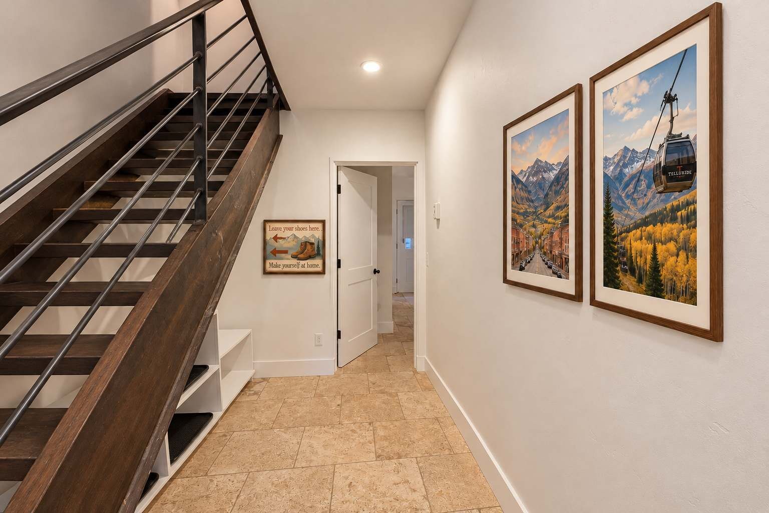 Una escalera con barandilla metálica que lleva a una puerta, un pasillo con piso de baldosas y dos cuadros en la pared.