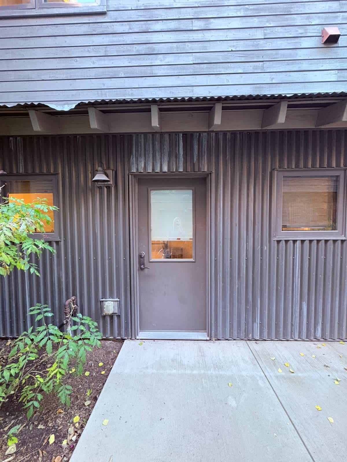 Un edificio con una puerta gris, un ventanal pequeño y un buzón de metal.