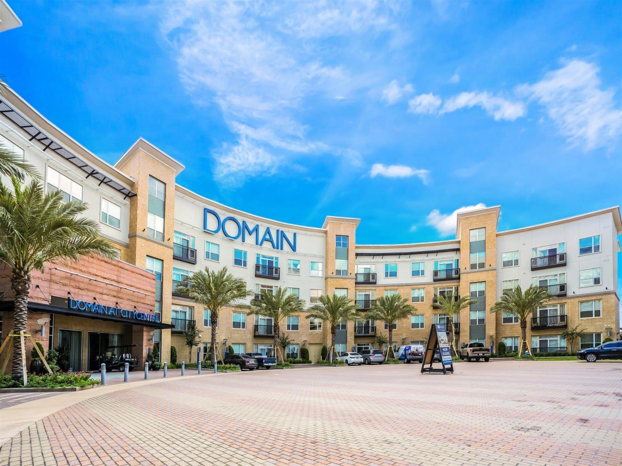 A multi-story hotel with a prominent 'DOMAIN' sign, a paved courtyard, and palm trees.