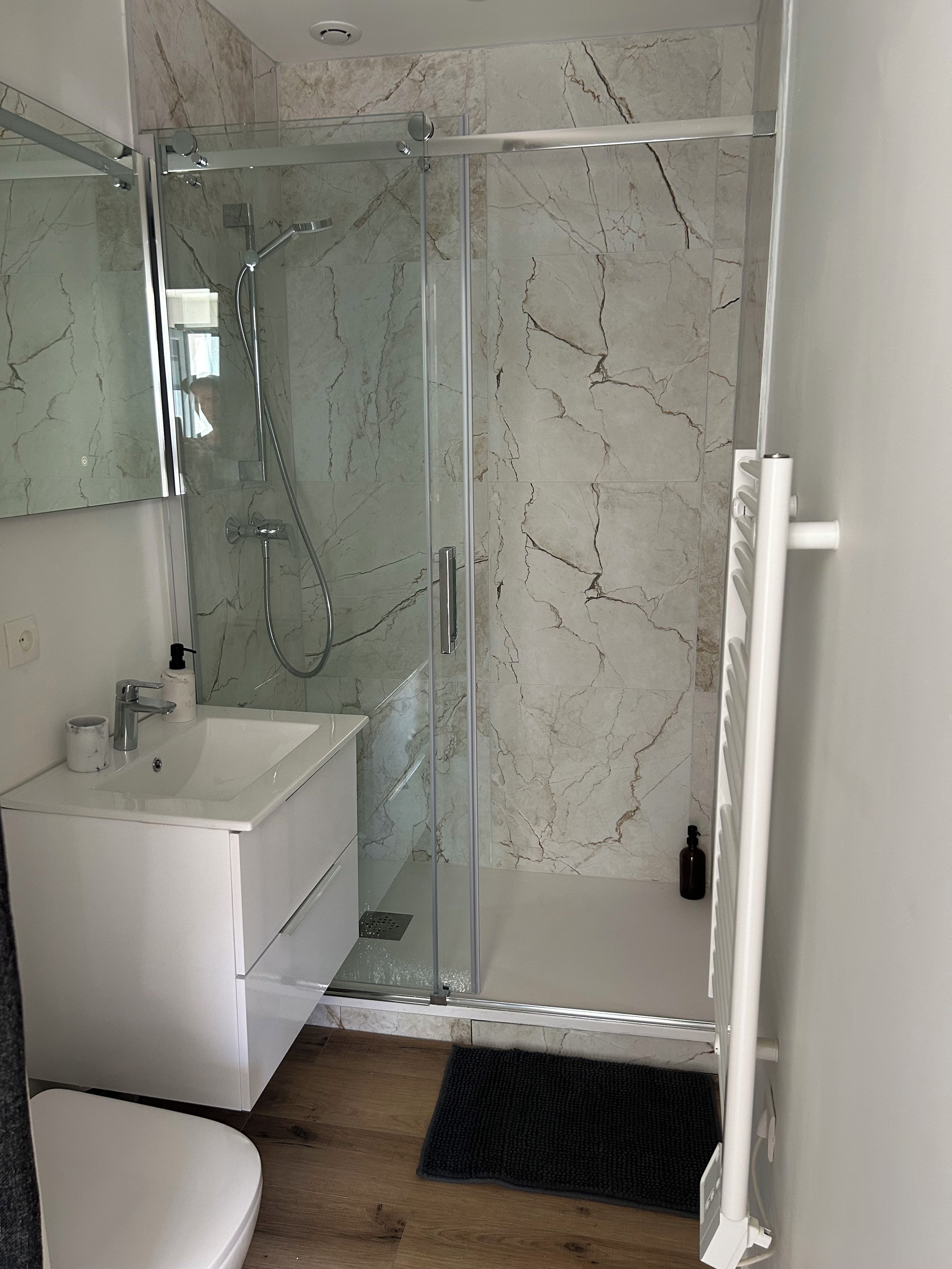 Een moderne badkamer met een glazen douchecabine, een wit wastafelmeubel en een wand betegeld met marmer.