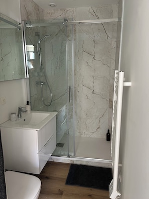 Un bagno moderno con doccia vetro, lavandino bianco e parete rivestita in marmo.