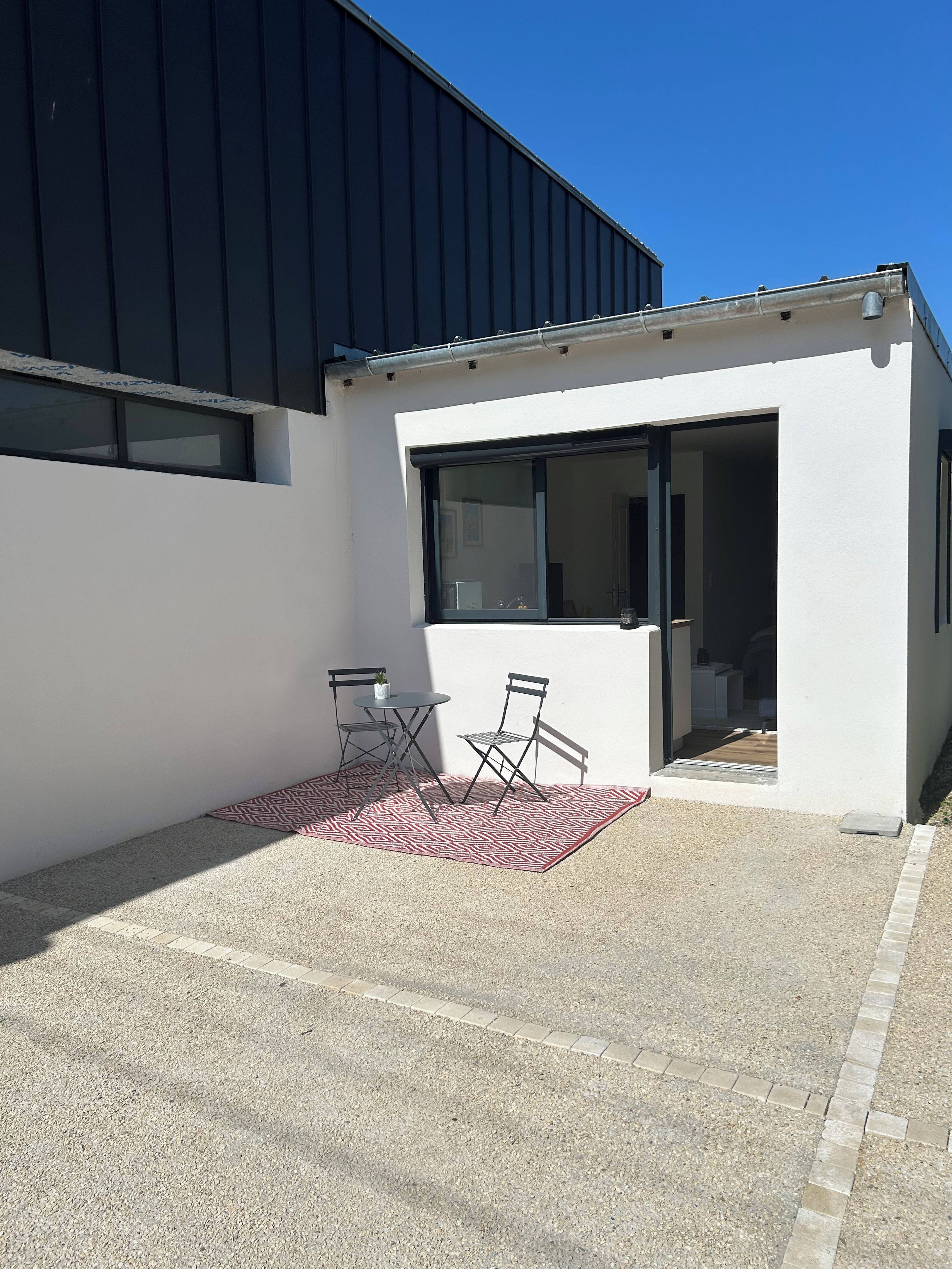 Een modern gebouw met een plat dak, een groot raam en een klein terras met een tafel en stoelen.