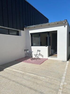 Un edificio moderno con tetto piatto, un'ampia finestra e un piccolo patio con tavolo e sedie.
