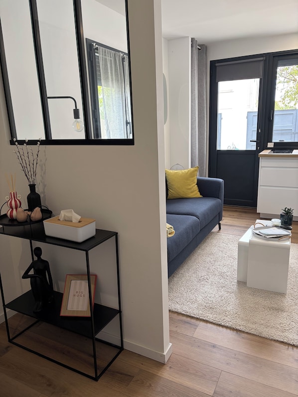 Ett modernt vardagsrum med en soffa, ett soffbord, ett sidobord, ett svart konsolbord med dekorativa föremål, en spegel och ett stort fönster med gardiner.