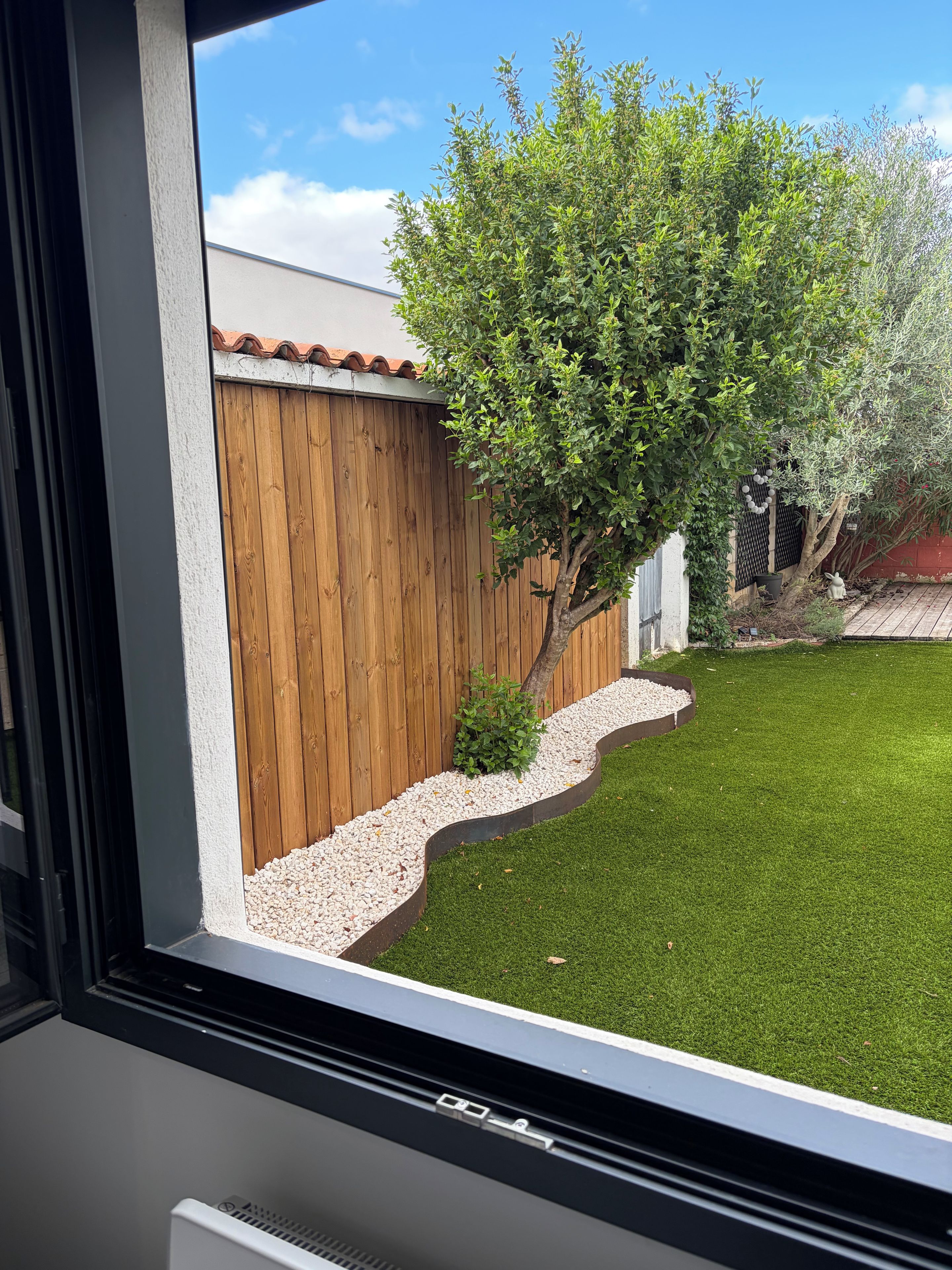 A view of a backyard with a wooden fence, a tree, and a grassy lawn.