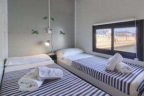 Ein Hotelzimmer mit zwei Einzelbetten, jeweils mit gestreifter Bettwäsche und Handtüchern. Ein Fenster bietet einen Blick nach draußen, und eine Wandleuchte ist angebracht.