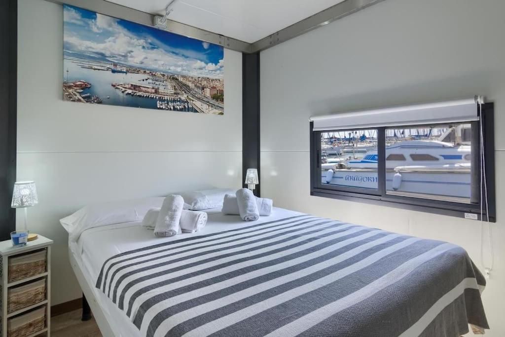 A hotel room with a bed, a window with a view of boats, a painting on the wall, and a nightstand with a lamp.