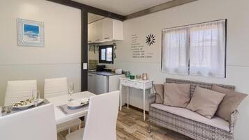 A dining area with a table set for two, a sofa, and a kitchen in the background.