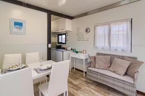 A dining area with a table set for two, a sofa, and a kitchen in the background.