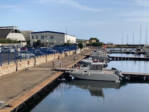 A marina with boats docked, a building with a blue roof, and a stone wall.