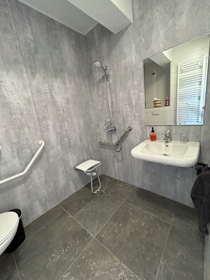 A bathroom with a shower, a sink, a toilet, and a small step stool. - New Listing (Montenois)